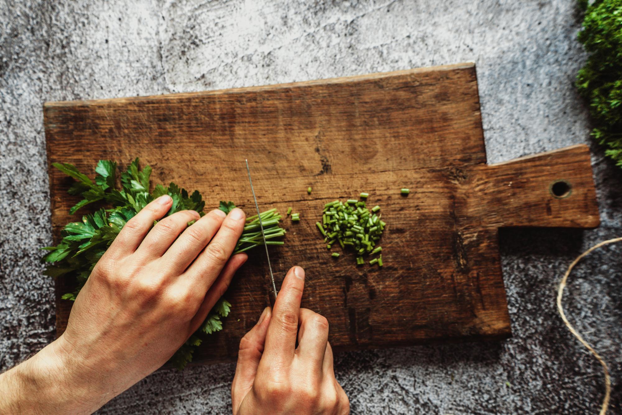 Close-up of hands chopping fresh herbs on a wooden board